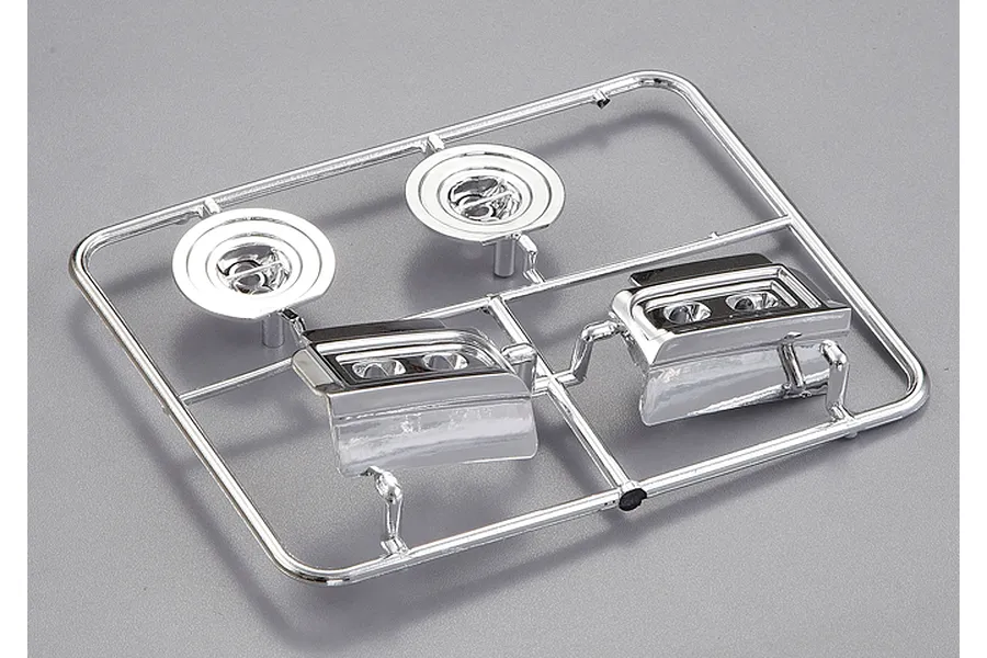 A chrome-plated plastic parts tree for a 1/10 scale RC car, featuring two circular light buckets and two rectangular headlight assemblies.
