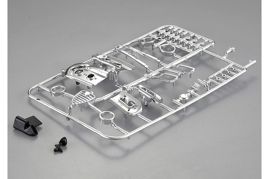 A chrome-plated plastic parts tree for an RC car model, including grille and light bucket components, alongside two small black plastic parts.
