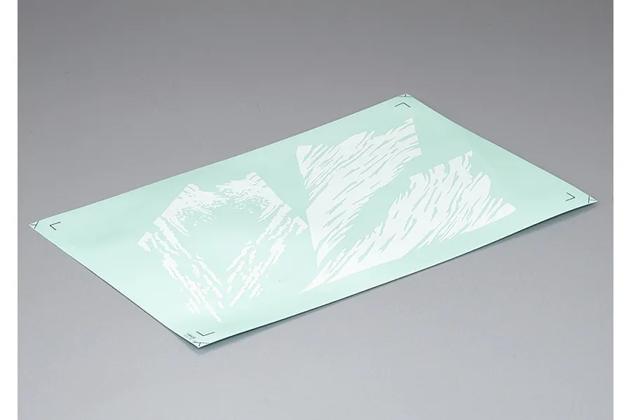 A rectangular sheet of white decals with abstract camouflage-like patterns on a light green backing paper, set against a plain grey background.