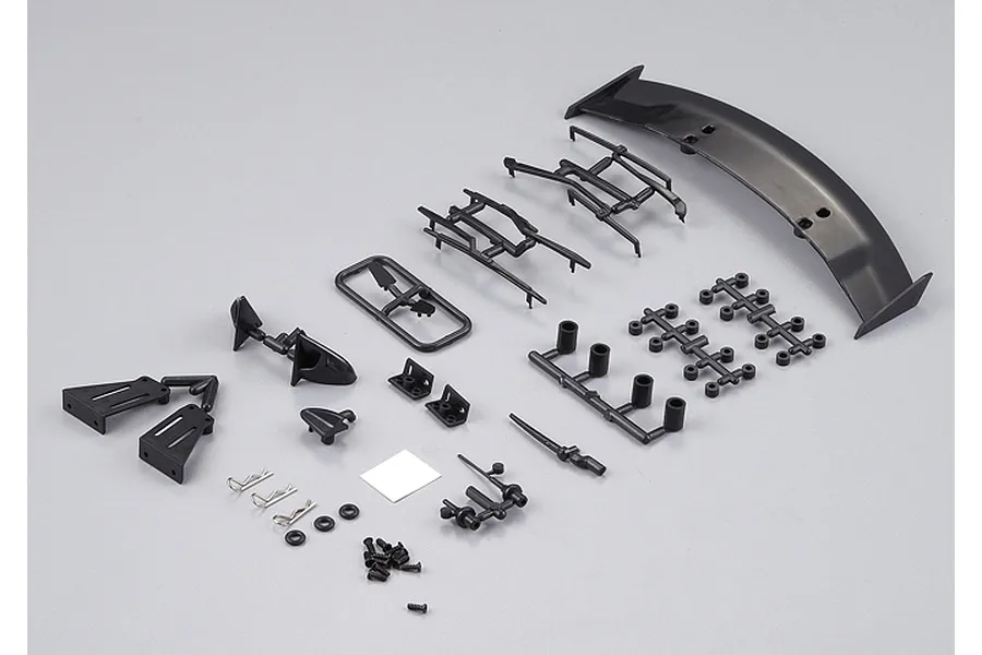 An assortment of black plastic RC car body accessories including a rear spoiler, side mirrors, mounting brackets, and small hardware on a grey background.