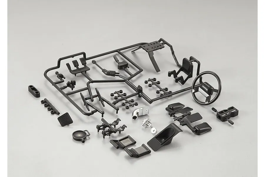 A set of black plastic model cockpit parts for an RC crawler on a grey background.