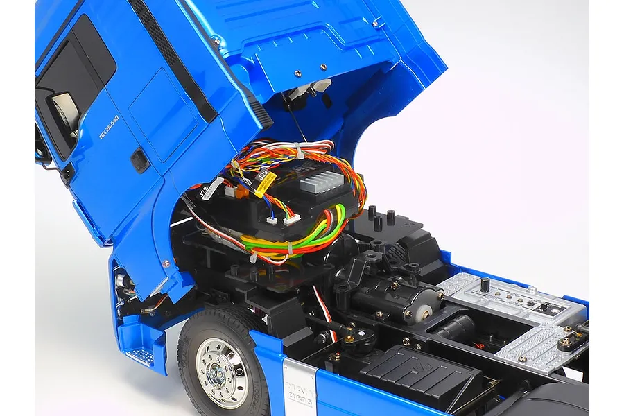 Close-up of a Tamiya MAN TGX 26.540 RC truck with the cab tilted forward to reveal the internal wiring, electronics, and chassis details.