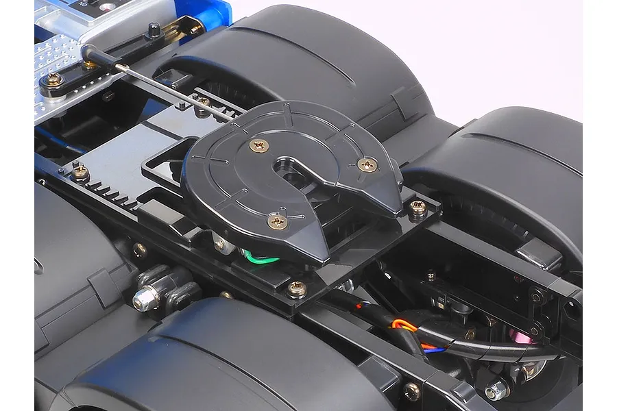 Close-up of the fifth wheel hitch assembly on a Tamiya 1/14 scale RC semi-truck chassis, showing black plastic fenders and metal frame components.