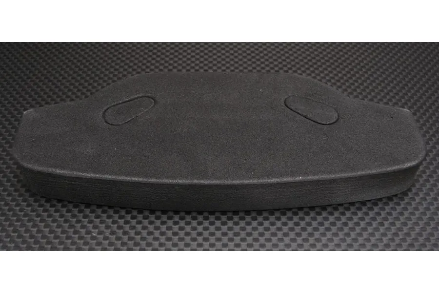 A black urethane foam bumper for an RC car, viewed from above against a carbon fiber pattern background.