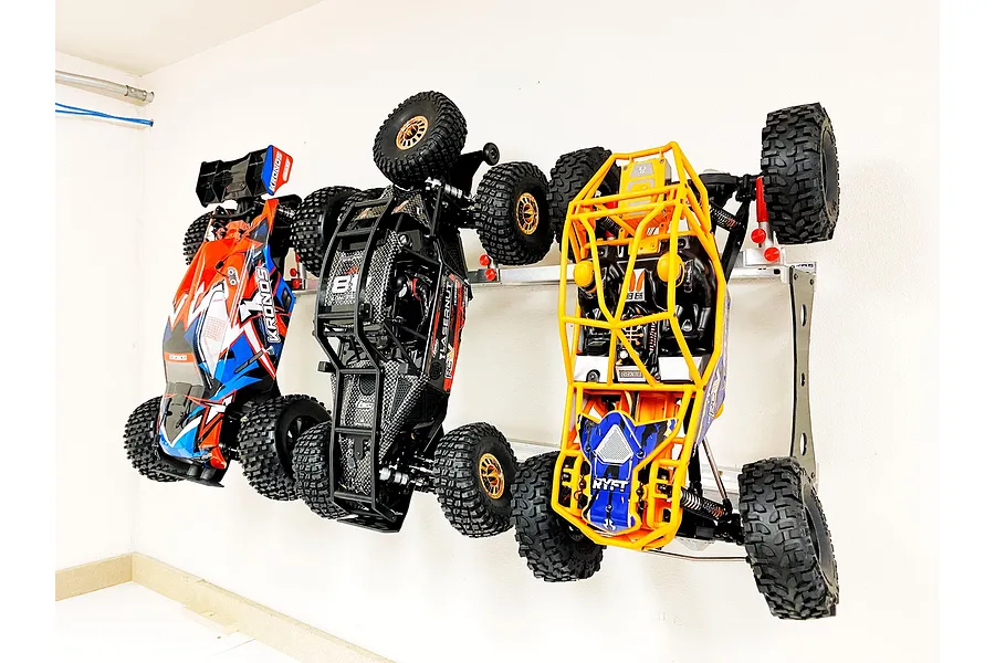 Three RC cars mounted vertically on a metal wall rack against a white wall.