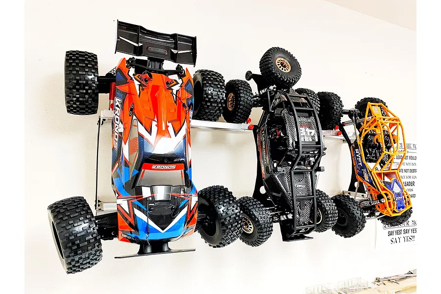 Three RC cars mounted vertically on a wall using T-Bone RC wall racks, showing a Corally Kronos, a Losi Lasernut, and an Axial Ryft.
