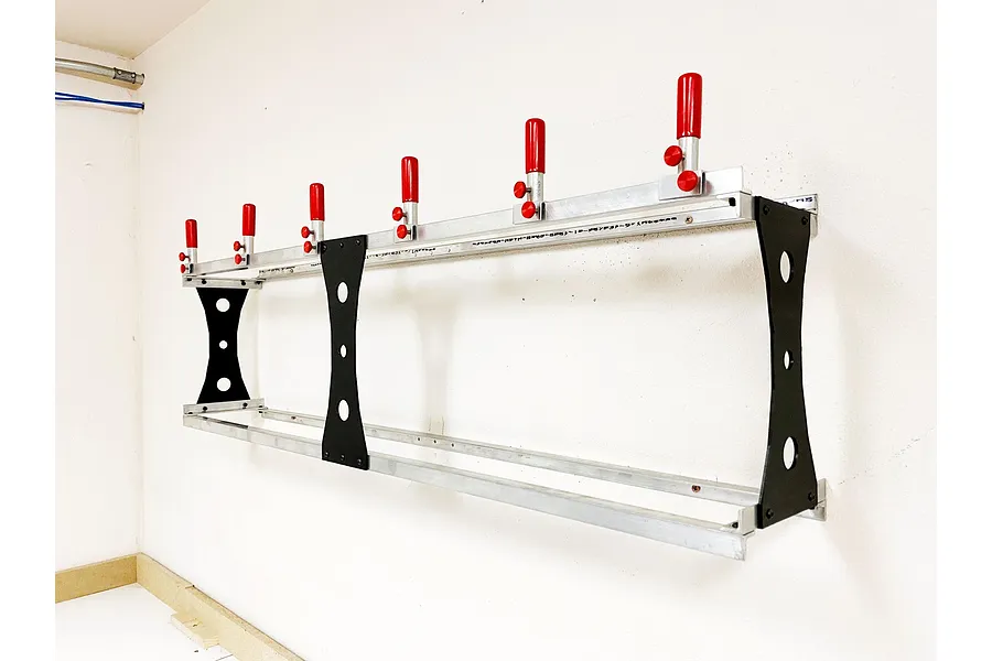 A T-Bone RC car wall rack mounted on a white wall, featuring aluminum rails, black side supports, and five adjustable red-tipped pegs.