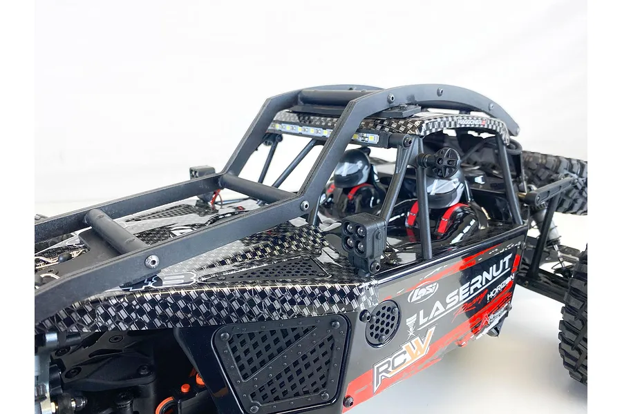 Close-up of a T-Bone Racing external roll cage installed on a Losi Lasernut RC car, showing the black frame, LED light bar, and driver figures.