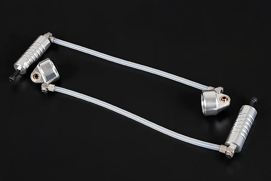 Two silver aluminium RC shock caps with attached external reservoirs connected by clear tubing on a black background.