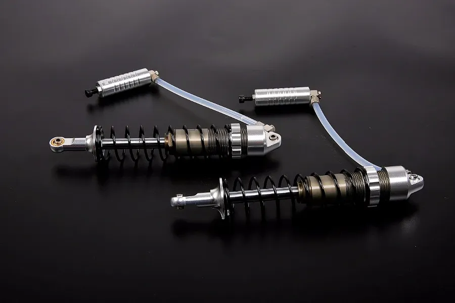 Two silver Rovan heavy-duty RC rear shock absorbers with external reservoirs connected by clear tubing, set against a dark background.