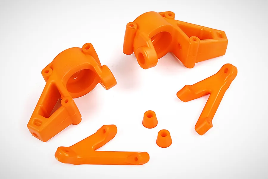 A set of bright orange nylon RC steering components including two steering hubs, two steering arms, and two small bushings on a white background.