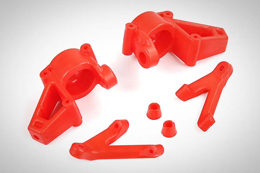 A set of bright red nylon RC car front steering hubs and suspension components on a white background.