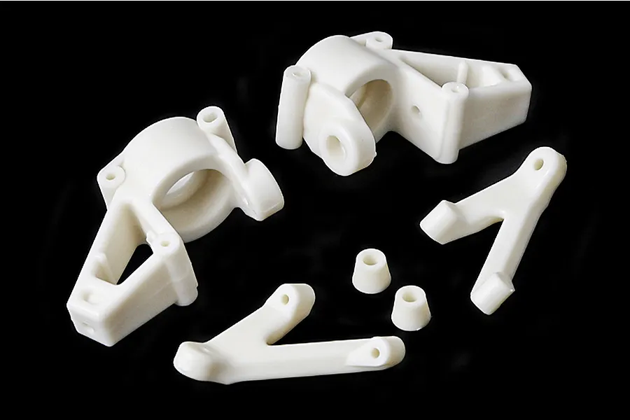 A set of white plastic RC steering hub components and suspension arms arranged on a black background.