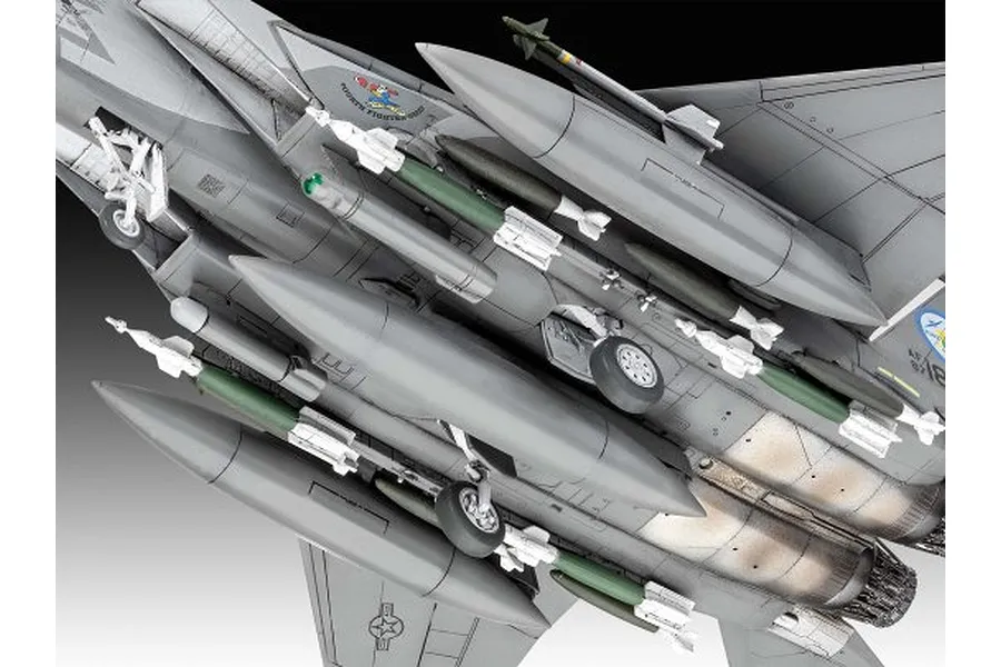 Underside view of a detailed F-15E Strike Eagle plastic model kit showing landing gear, fuel tanks, and various missiles mounted on the wings and fuselage.