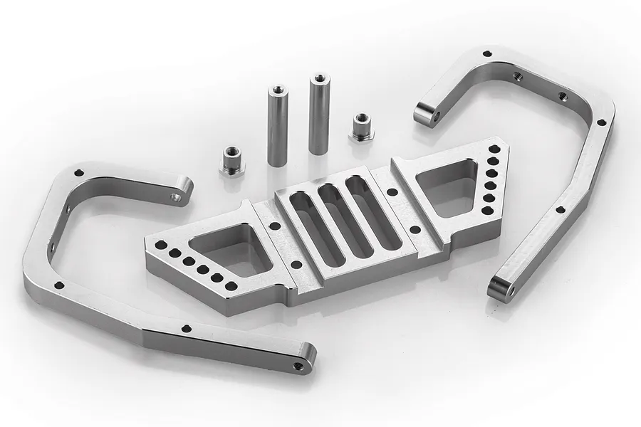 A silver aluminum rear bumper kit for an RC car, including a central bumper plate, two side support arms, two cylindrical spacers, and two small nuts.