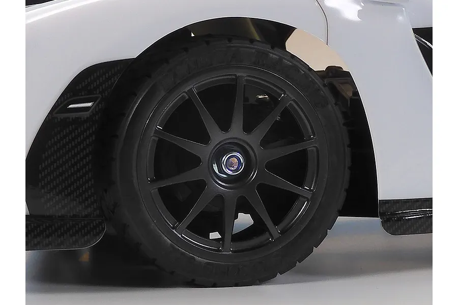 Close-up of a black multi-spoke wheel on a white Tamiya RC car with Tamiya Racing tire branding.