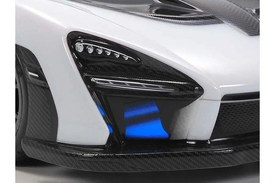 Close-up of the front headlight and bumper area of a white Tamiya McLaren Senna RC car body shell with carbon fiber detailing.