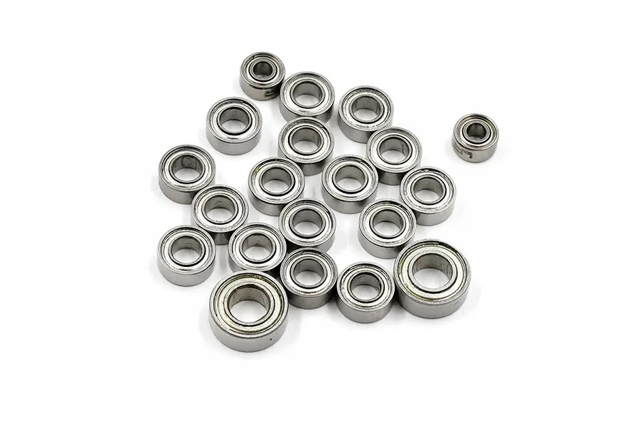 A collection of twenty small metal ball bearings of various sizes scattered on a white background.