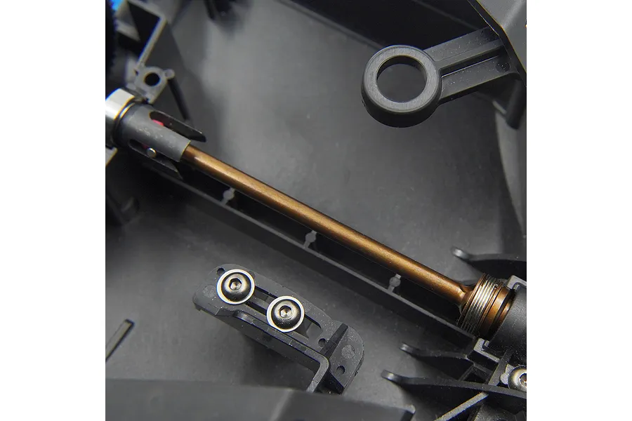 A close-up view of a bronze-colored metal driveshaft installed inside a black plastic RC car chassis.