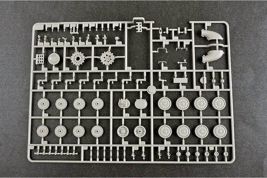 A grey plastic sprue containing various tank model parts, including road wheels, sprockets, and small mechanical components for a 1/35 scale model kit.