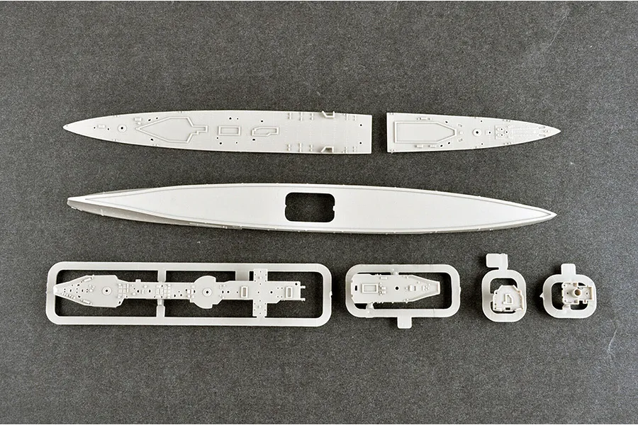 Top-down view of unpainted grey plastic model ship parts including hull sections and deck pieces on a dark grey surface.