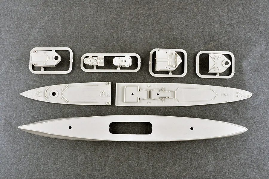 Top-down view of unpainted plastic model ship parts including the hull, deck sections, and small superstructure components on a grey surface.