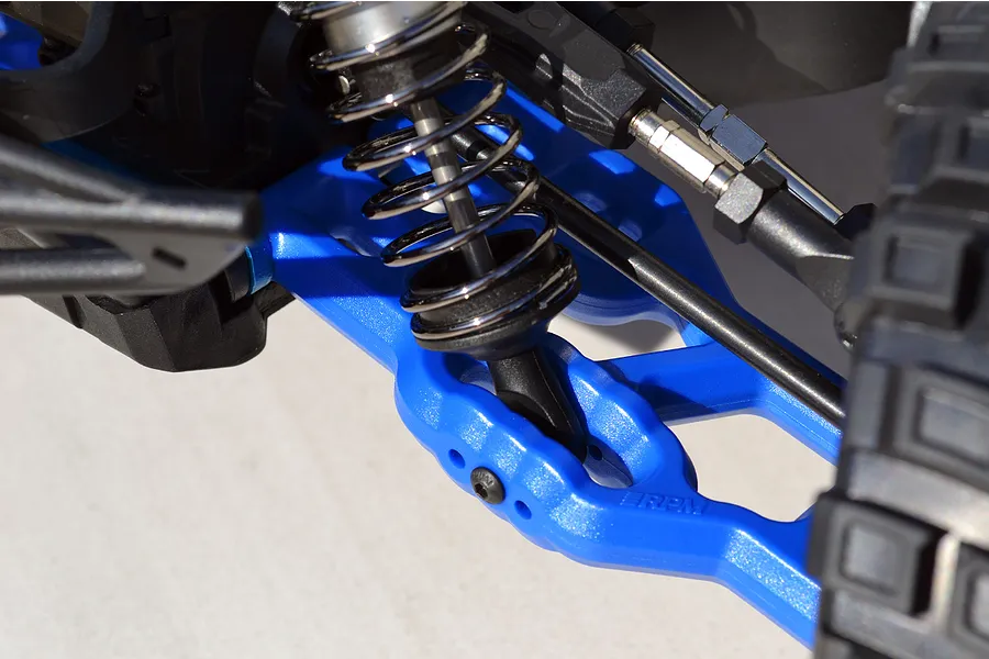 Close-up of a bright blue RPM suspension arm installed on an RC vehicle, featuring a metal coil-over shock absorber and black plastic components.