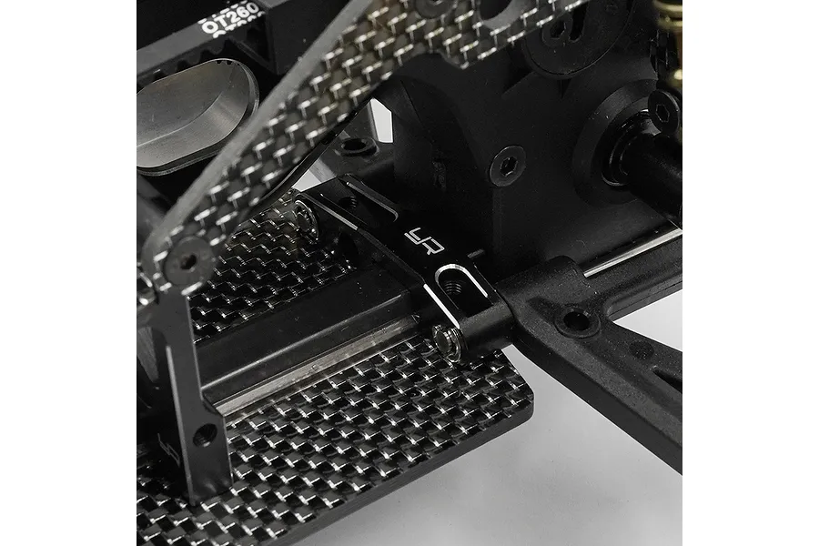 Close-up of a black aluminium Yeah Racing suspension arm pin brace installed on a carbon fibre RC car chassis.