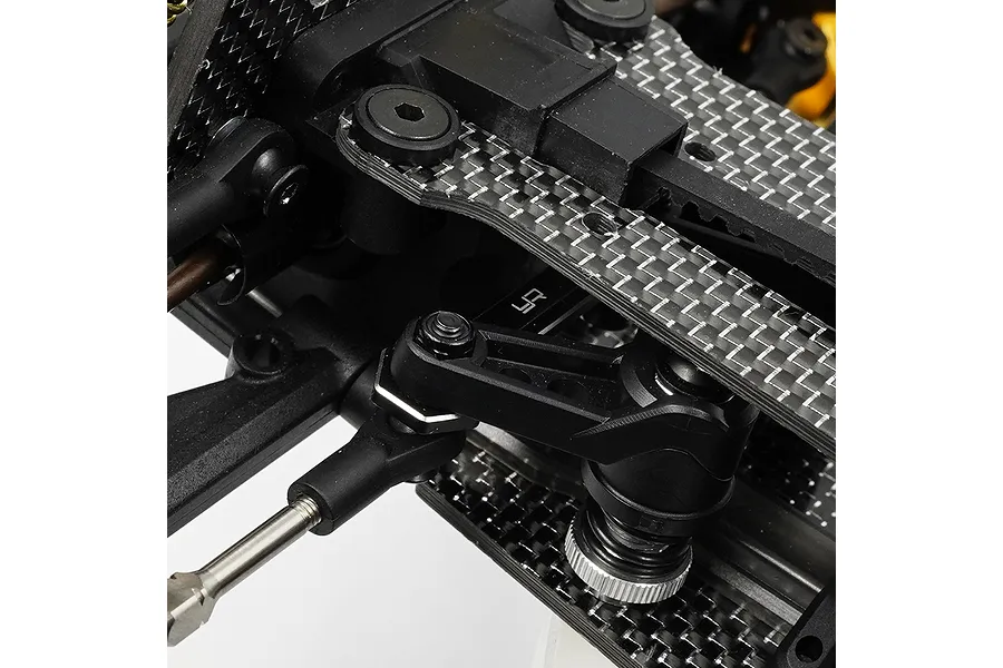 Close-up of a black aluminium steering brace installed on an RC car chassis with carbon fibre components.