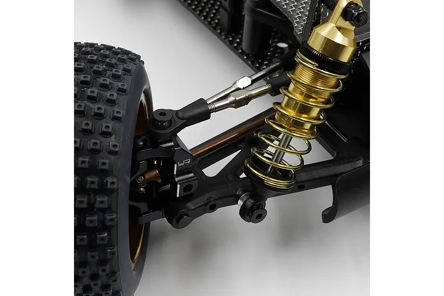 Close-up of a Yeah Racing RC car suspension assembly featuring a gold-anodized shock absorber, black plastic control arms, and a knobby rubber tire.