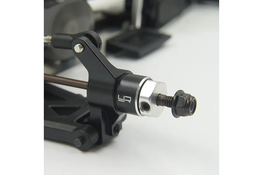 Close-up of a black anodized aluminum RC steering knuckle with a silver wheel hex adapter installed on a model car suspension arm.