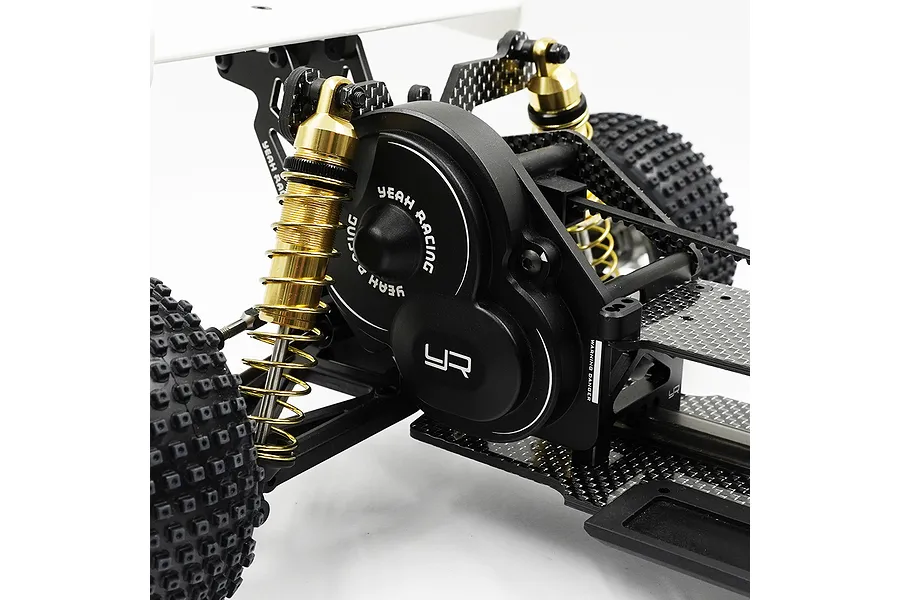A close-up view of a black aluminium Yeah Racing gearbox cover installed on an RC buggy chassis, featuring gold shock absorbers and carbon fibre components.