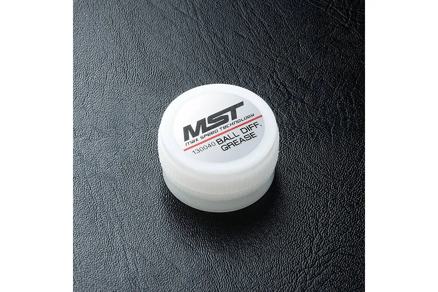 A small white plastic container of MST Ball Differential Grease, model 130040, sitting on a black textured surface.