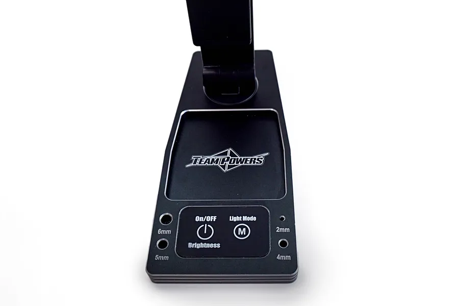 Close-up of the base of a black Team Powers LED pit light, showing the control panel with On/Off, Brightness, and Light Mode buttons and tool storage holes.