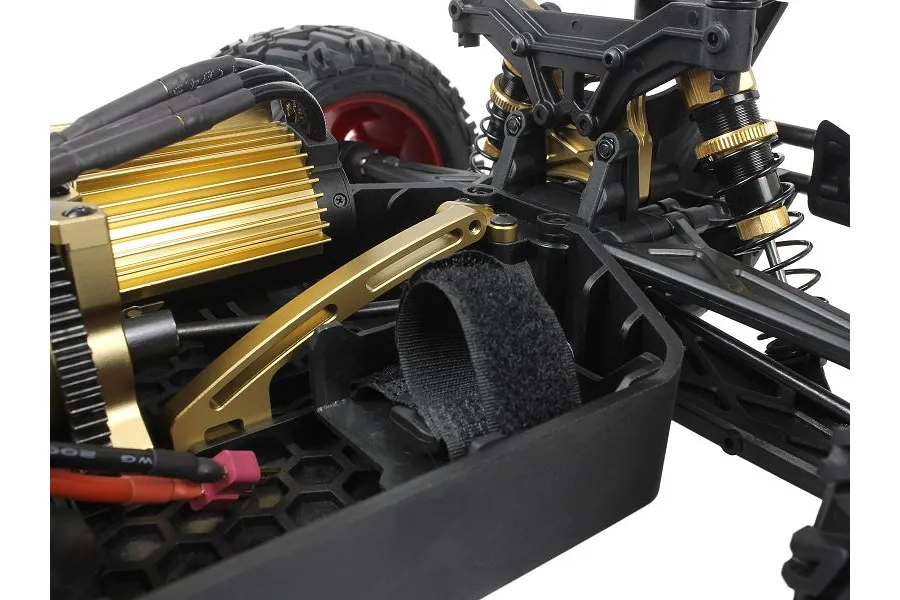 Close-up of a gold aluminium chassis brace installed on a Maverick RC car, showing the motor, shock towers, and battery strap.
