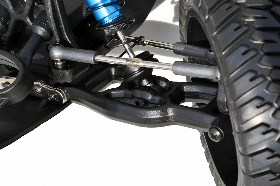 Close-up of a black RPM front lower suspension arm installed on an RC vehicle, showing the shock absorber, steering linkage, and wheel.