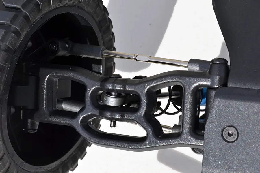 Close-up of an RPM front lower suspension arm installed on an RC vehicle, showing the black plastic arm, wheel, and steering linkage.