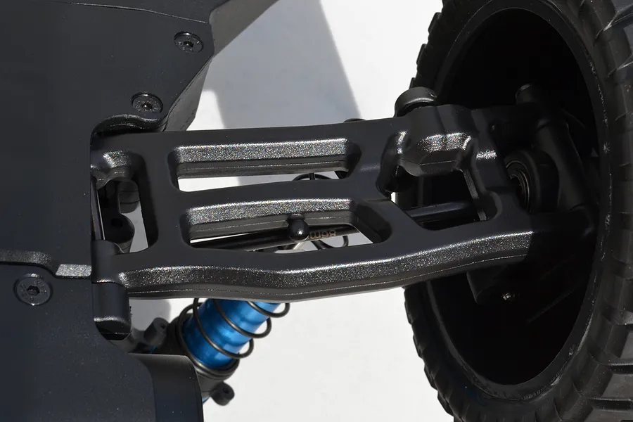Close-up of an RPM black rear lower suspension arm installed on an RC vehicle chassis with a blue shock absorber and black wheel.