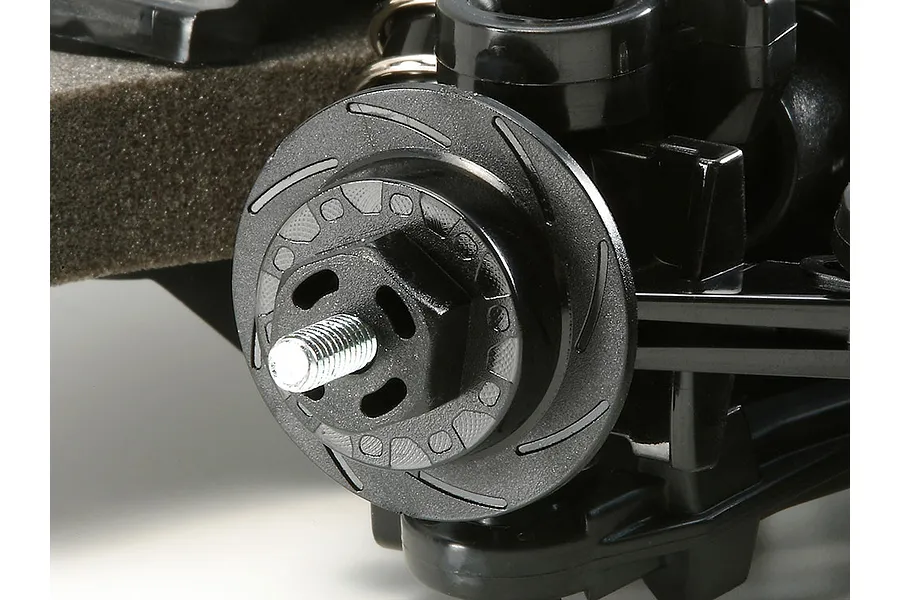 Close-up of a Tamiya TT-02 RC car wheel hub and brake disc detail on a black plastic suspension arm.