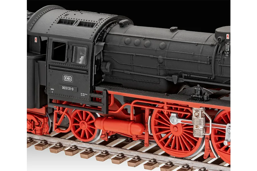 Close-up of a 1/87 scale plastic model steam locomotive with a matte black boiler and bright red wheels on a model railway track.