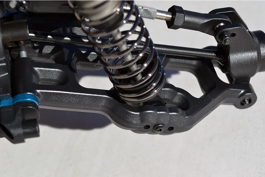 Close-up of an RPM black plastic rear suspension arm installed on an RC vehicle, featuring a coil-over shock absorber and metal hardware.