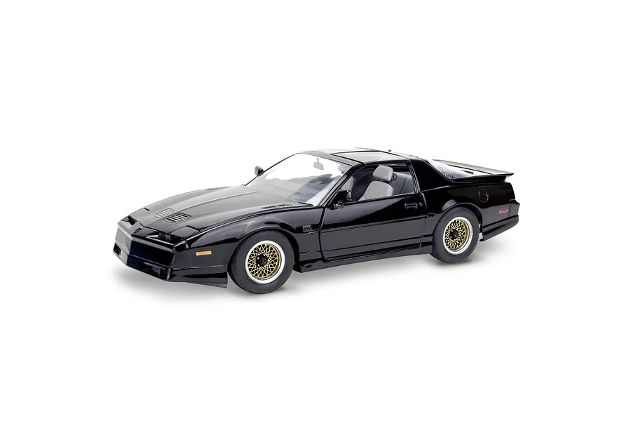A high-angle studio shot of a black 1987 Pontiac Firebird GTA model car with gold cross-lace wheels against a white background.