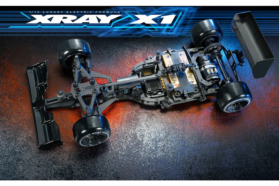 Top-down view of an XRAY X1 1/10 scale electric formula RC car kit chassis, featuring carbon fiber components, black wheels, and electronic components.