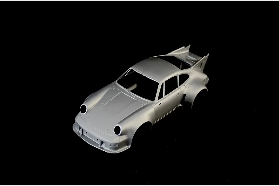 Unpainted grey plastic model car body of a Porsche Carrera RSR Turbo on a black background.