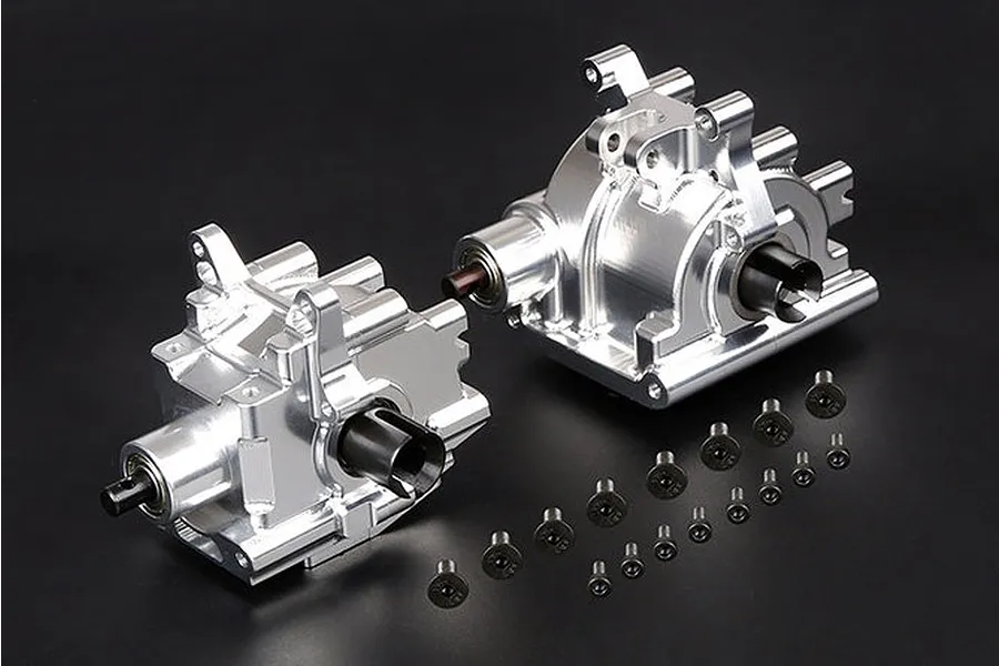 Two silver aluminium RC gearbox housings with black drive cups and a collection of small black screws on a black background.