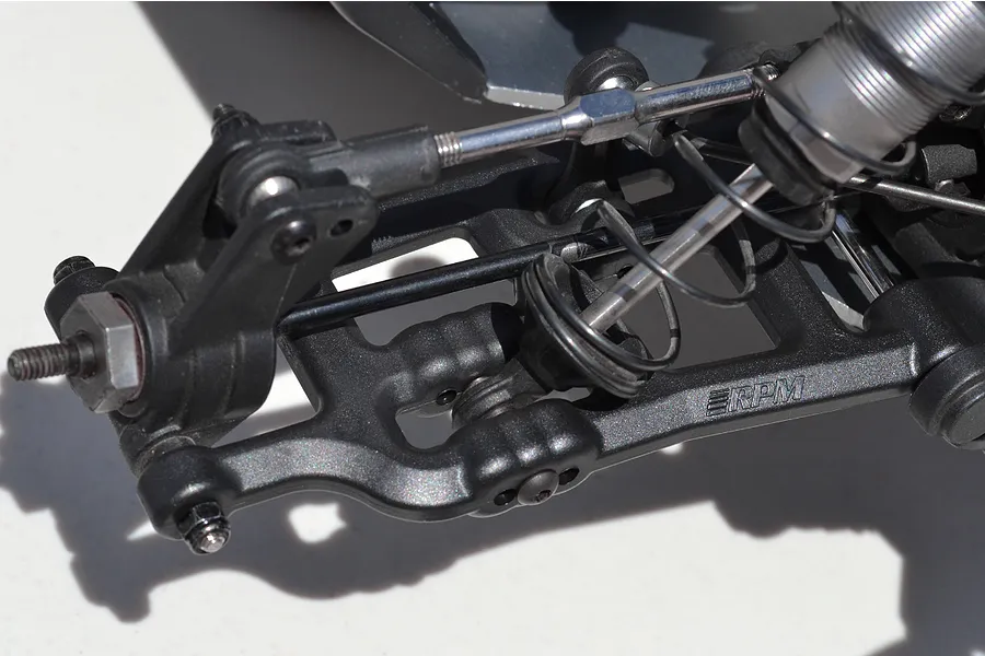 Close-up of an RPM black plastic rear suspension arm installed on an RC vehicle, showing the shock absorber and steering linkage.