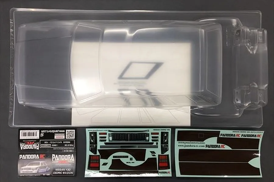 An unpainted clear polycarbonate RC car body shell for a Nissan Cedric Wagon, including decal sheets and packaging, viewed from above.