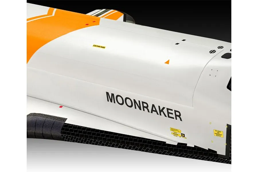 Close-up of the fuselage of a Moonraker space shuttle model kit, showing white and orange paint, black thermal tiles, and Moonraker branding.