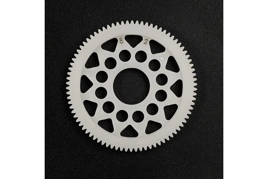 A white Delrin 82T 64dp spur gear for RC cars, featuring a circular design with weight-reduction holes, centered on a black background.