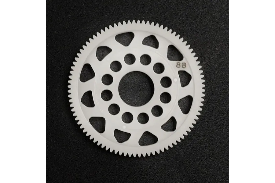 A white Delrin 88T spur gear for RC cars, featuring a lightweight design with circular and triangular cutouts, set against a dark textured background.